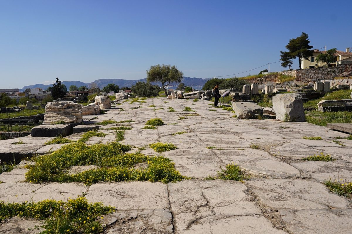 Pavimento de piedra y restos arqueológicos del Telesterión, el santuario donde se celebraban los Misterios de Eleusis, con una visitante observando las ruinas