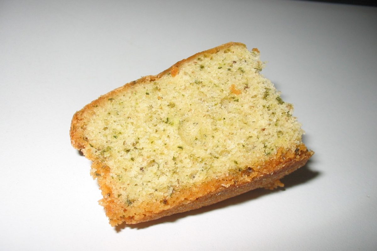 Rebanada de bizcocho casero con motas verdes de cannabis visibles en la miga, sobre fondo blanco