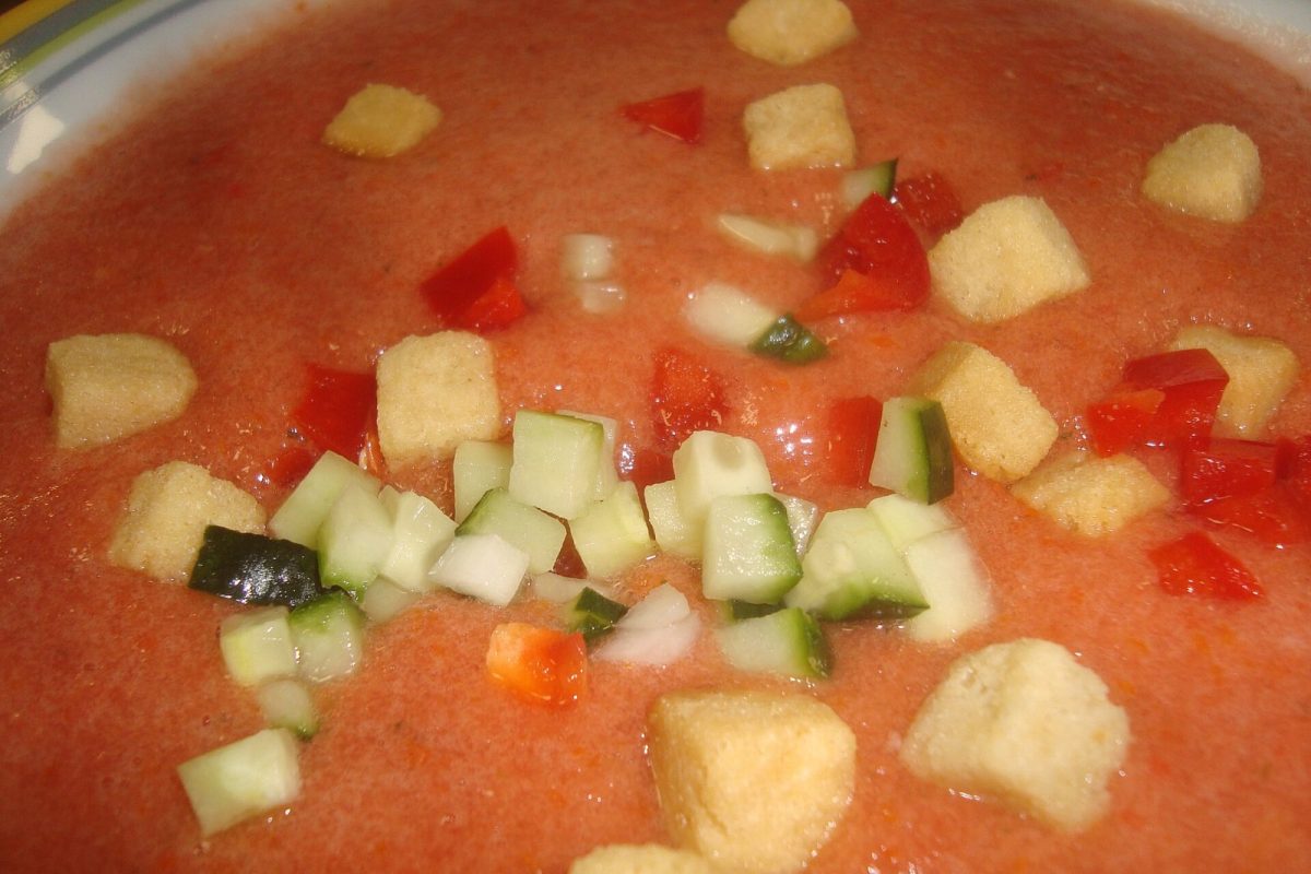 Primer plano de un cuenco de gazpacho frío con tropezones de pepino, pimiento, cebolla y picatostes
