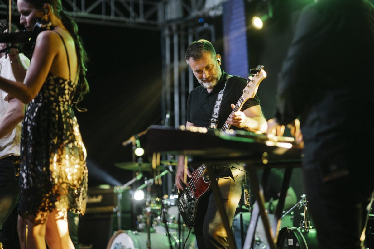 Músicos tocando el bajo y otros instrumentos sobre un escenario iluminado con luces verdes durante un concierto nocturno
