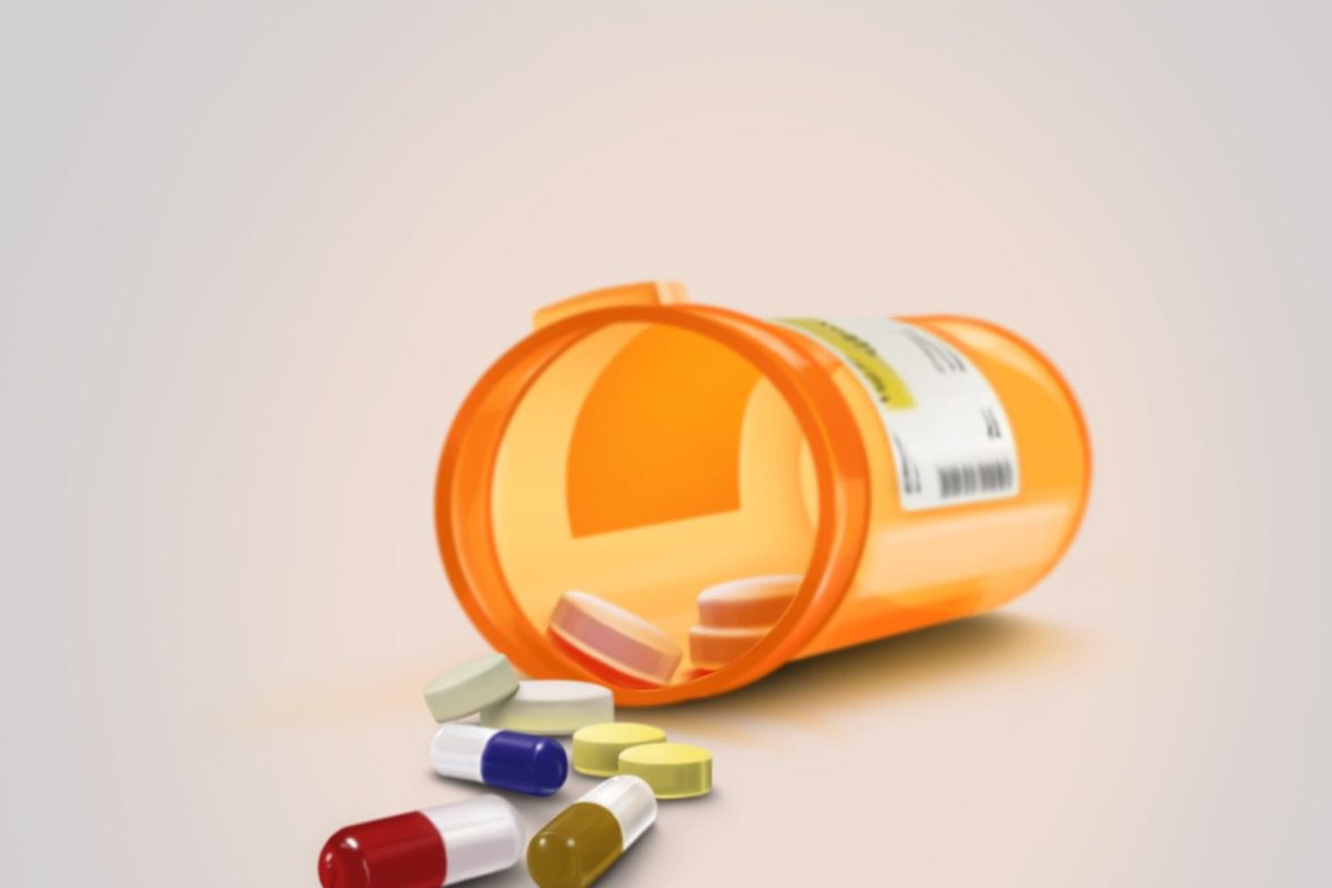 Bote naranja de medicamentos volcado con cápsulas y pastillas de colores esparcidas sobre una superficie clara