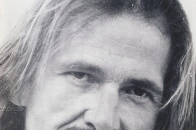 Retrato en blanco y negro de un hombre de pelo largo y bigote, mirando a cámara con expresión seria