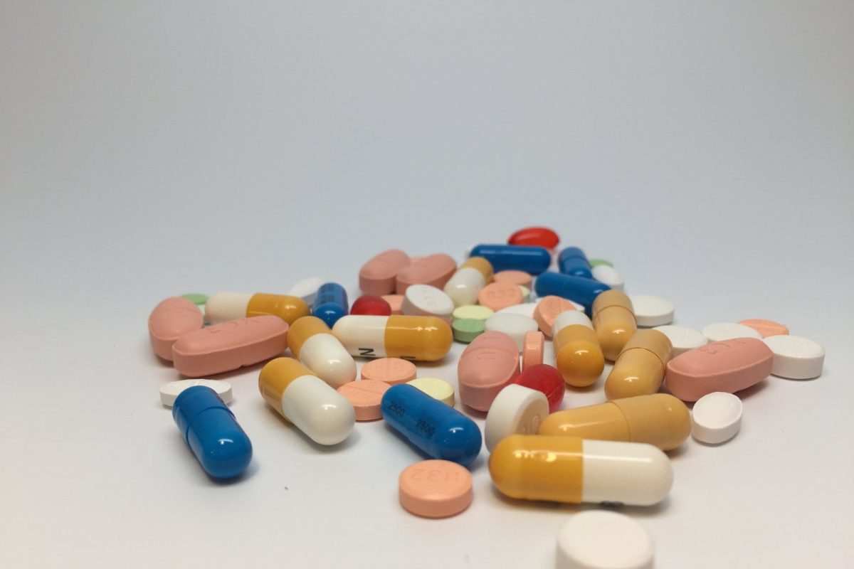 Montón de pastillas y cápsulas de distintos colores y formas esparcidas sobre una superficie blanca