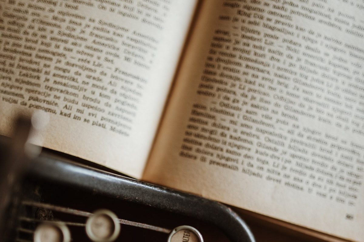 Máquina de escribir vintage junto a un libro abierto sobre una mesa de madera, evocando la escritura de una carta