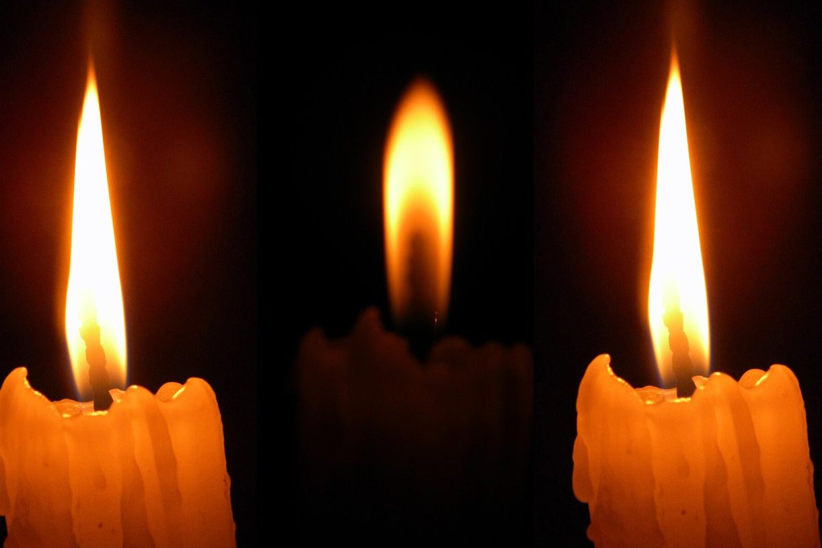 Tres llamas de vela encendidas destacando sobre un fondo completamente oscuro, en tono contemplativo