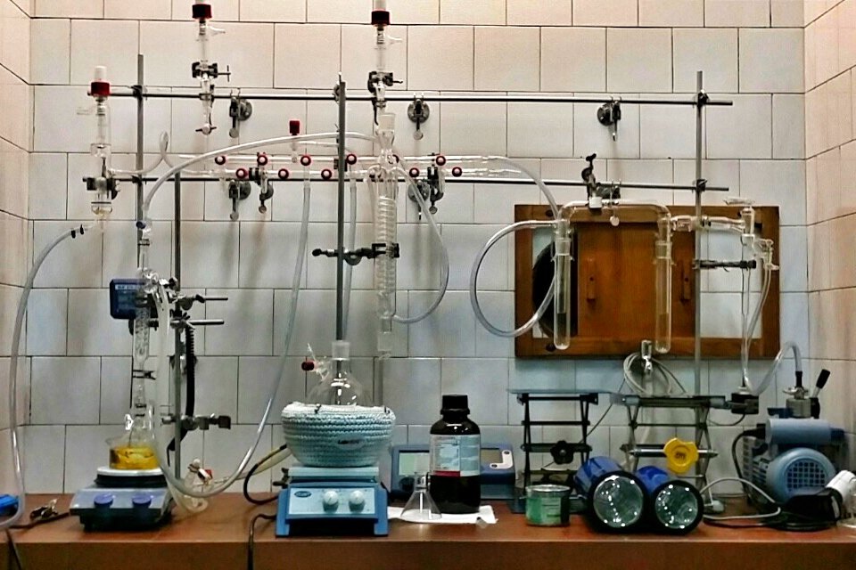 Equipo de destilación y reflujo de vidrio con un frasco ámbar, montado contra una pared de azulejos en un laboratorio de química