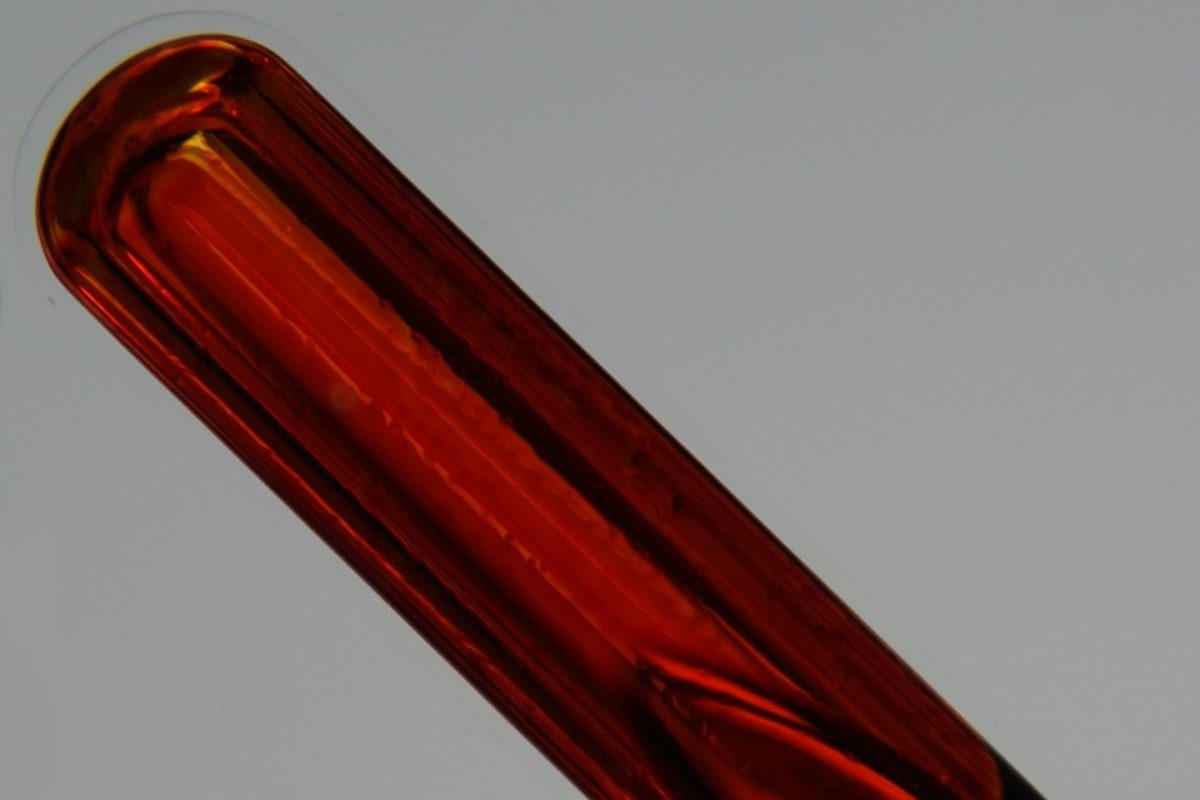 Vial de vidrio sellado con bromo líquido puro, de color rojo anaranjado intenso, fotografiado en primer plano