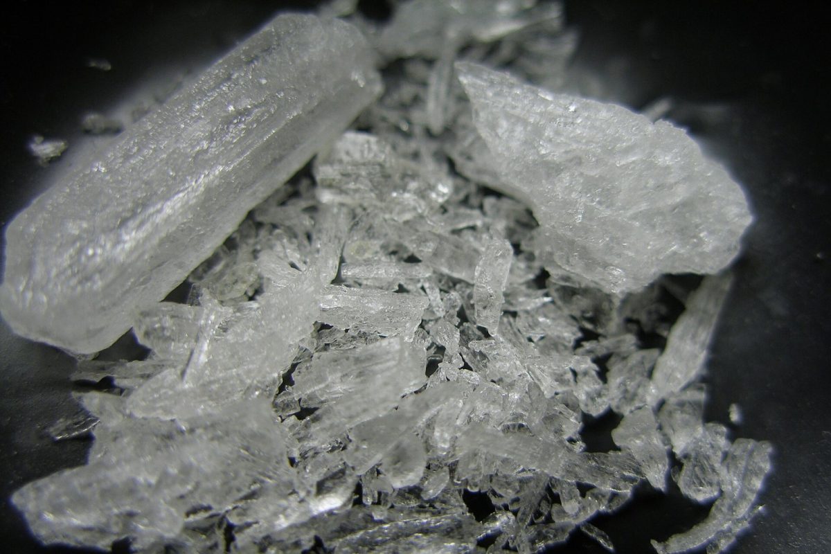 Primer plano macro de fragmentos y cristales translúcidos de metanfetamina sobre fondo oscuro