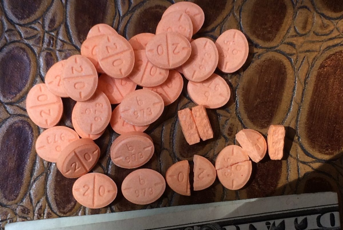 Conjunto de comprimidos ovalados de color naranja, sales de anfetamina de uso farmacéutico, fotografiados de cerca junto a un billete para escala.