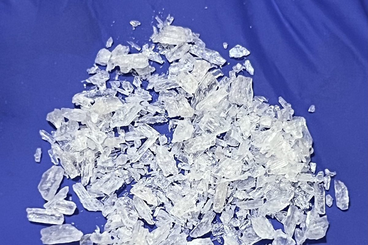 Montón de fragmentos cristalinos translúcidos de metanfetamina sobre un fondo de tela azul.