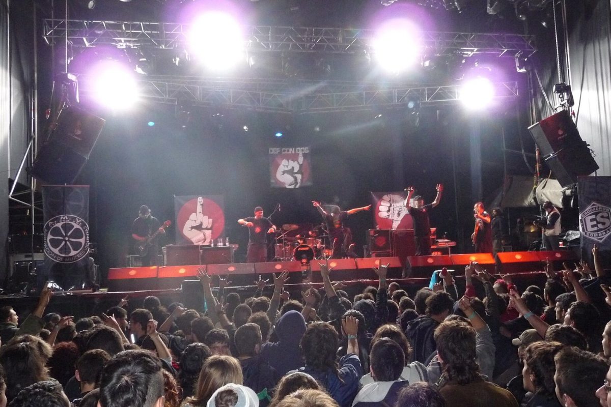 El grupo Def Con Dos actuando en directo sobre un escenario iluminado, con el público levantando los brazos