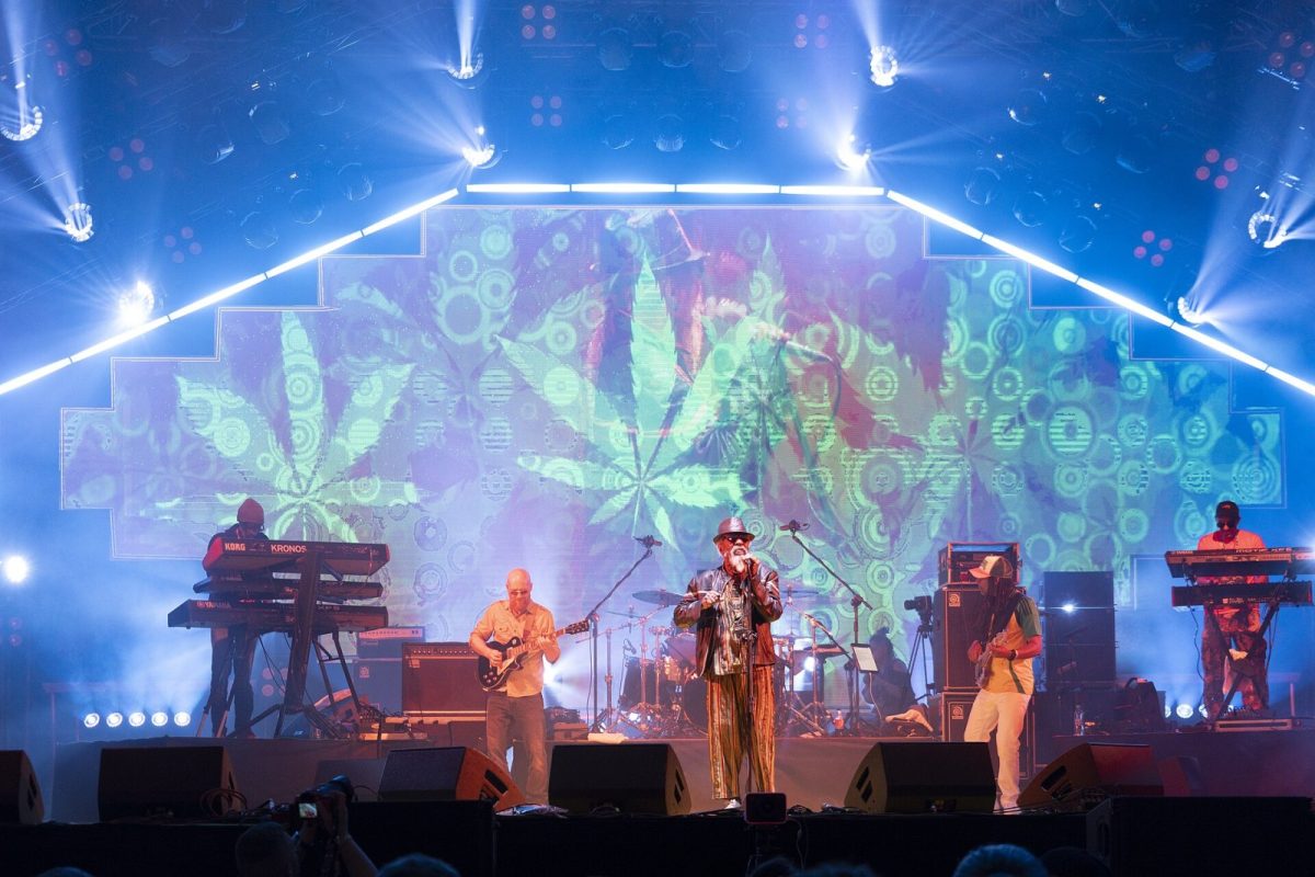 Banda de reggae actuando en un escenario con luces azules y una hoja de cannabis proyectada de fondo