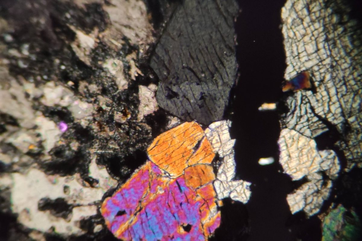 Cristales minerales de colores vivos e irregulares observados bajo un microscopio de luz polarizada