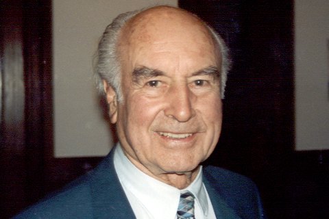 Albert Hofmann, hombre mayor calvo y sonriente, con traje azul y corbata, retratado en interior