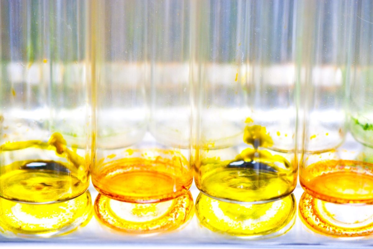Fila de tubos de ensayo de laboratorio con líquidos de colores amarillo, naranja y verde iluminados a contraluz