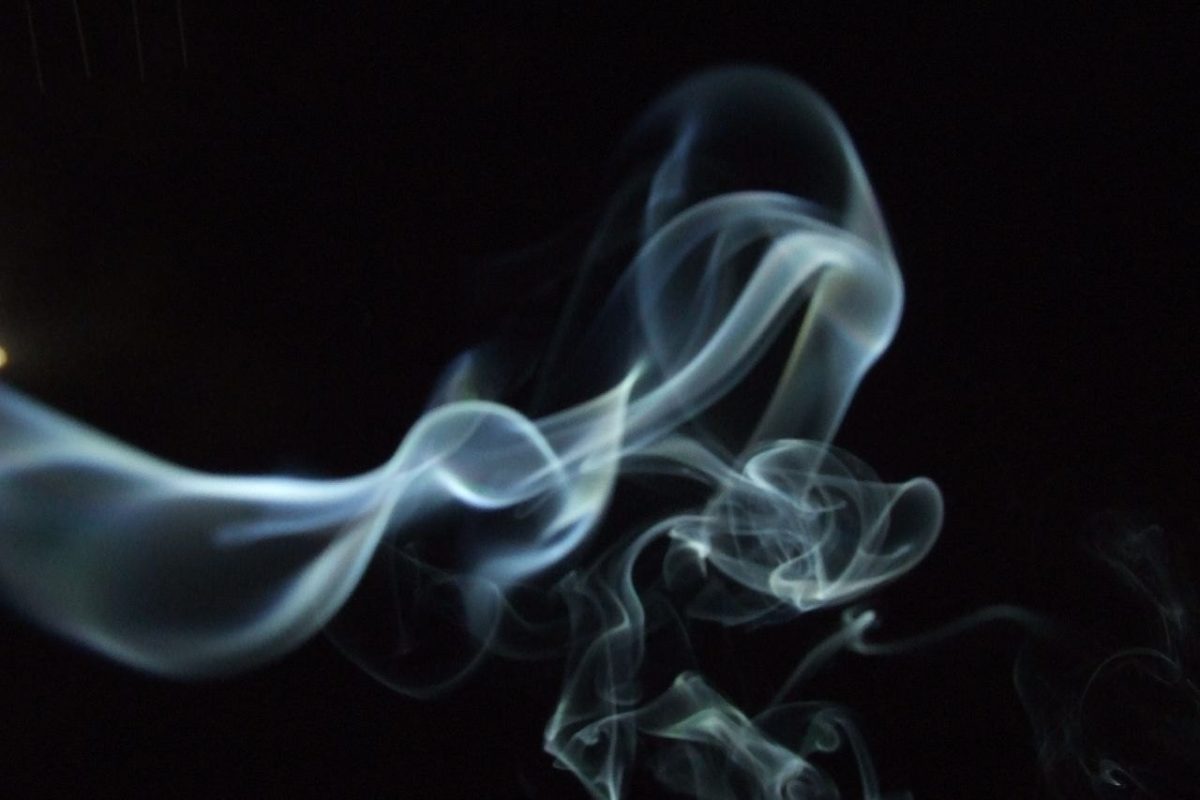 Volutas de humo de incienso blanco elevándose y formando espirales sobre un fondo completamente negro