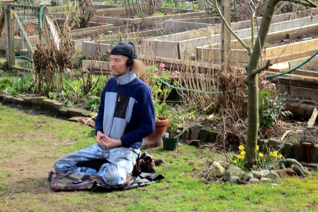 Hombre sentado en posición de meditación con auriculares en un jardín