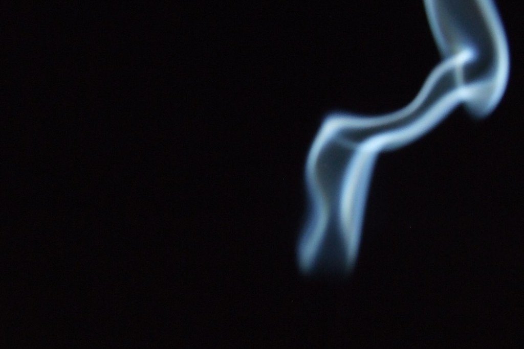 Voluta de humo de incienso ascendiendo sobre un fondo completamente negro