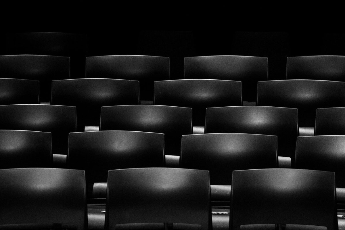 Filas de butacas de cine vacías en blanco y negro, iluminación tenue
