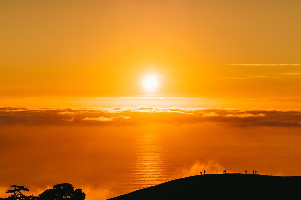 Grupo de personas en silueta sobre una cresta montañosa contemplando un amanecer anaranjado sobre un mar de nubes