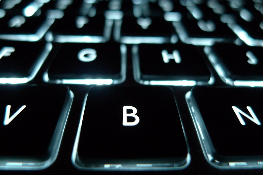 Primer plano de un teclado de portátil retroiluminado en un ambiente oscuro