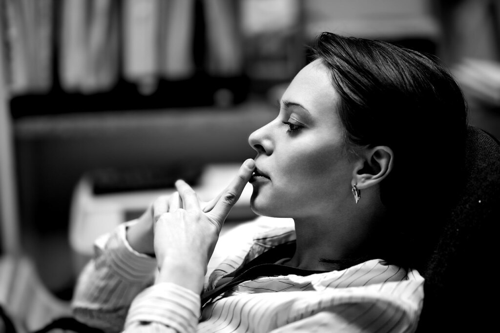 Mujer joven en actitud pensativa y preocupada, con los dedos cerca de la boca, mirando hacia un lado en una fotografía en blanco y negro