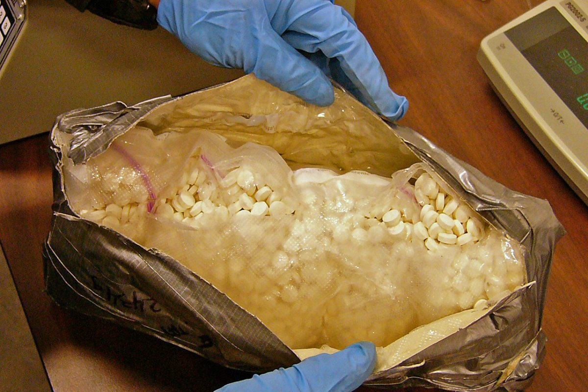 Manos con guantes de látex azul abriendo un paquete con miles de pastillas blancas de éxtasis incautadas