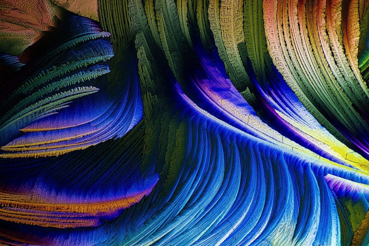 Cristales coloridos formando patrones en abanico bajo un microscopio de luz polarizada, en tonos azules, verdes y dorados