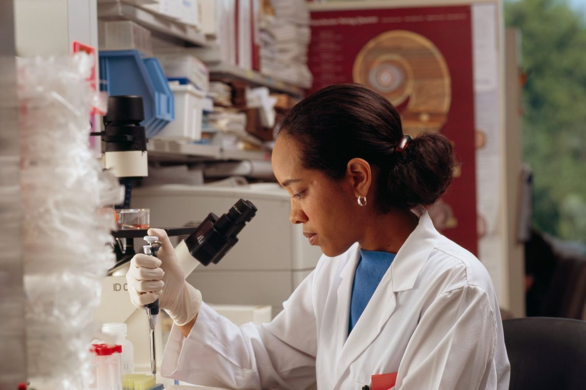 Científica con bata blanca usando una pipeta junto a un microscopio en un laboratorio de investigación