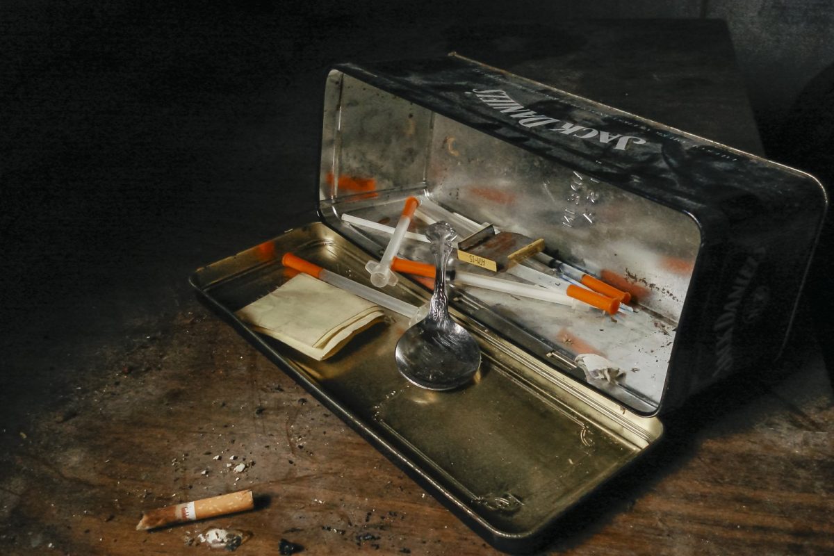 Jeringuillas, una cuchara y papel de fumar dentro de una lata metálica sobre una mesa de madera