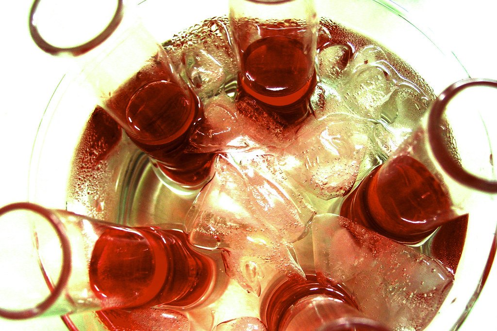 Vista cenital de varios vasos de chupito con licor rojo enfriándose entre cubitos de hielo