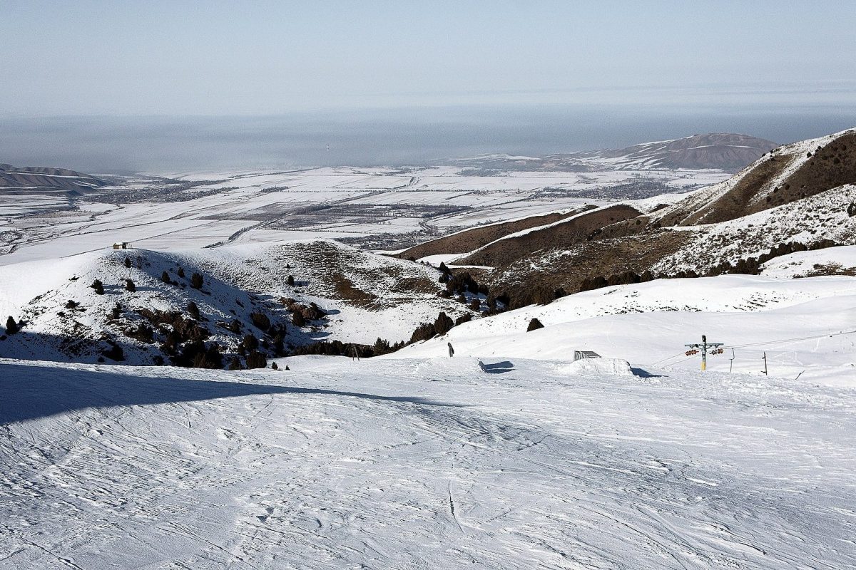 Pista de esquí nevada con remonte, con vistas a un valle y montañas al atardecer