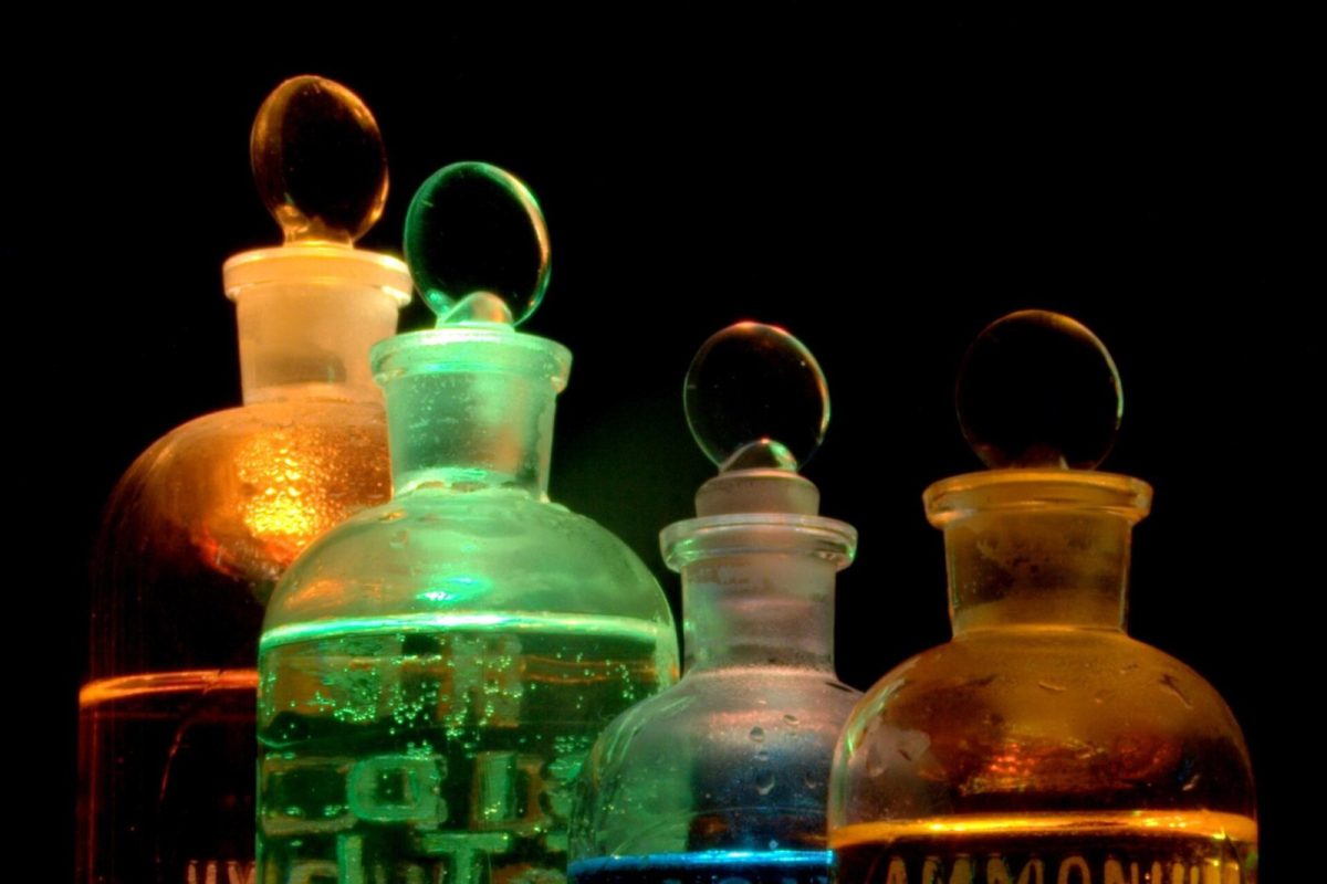 Frascos de vidrio de laboratorio con líquidos de colores brillantes iluminados sobre fondo oscuro