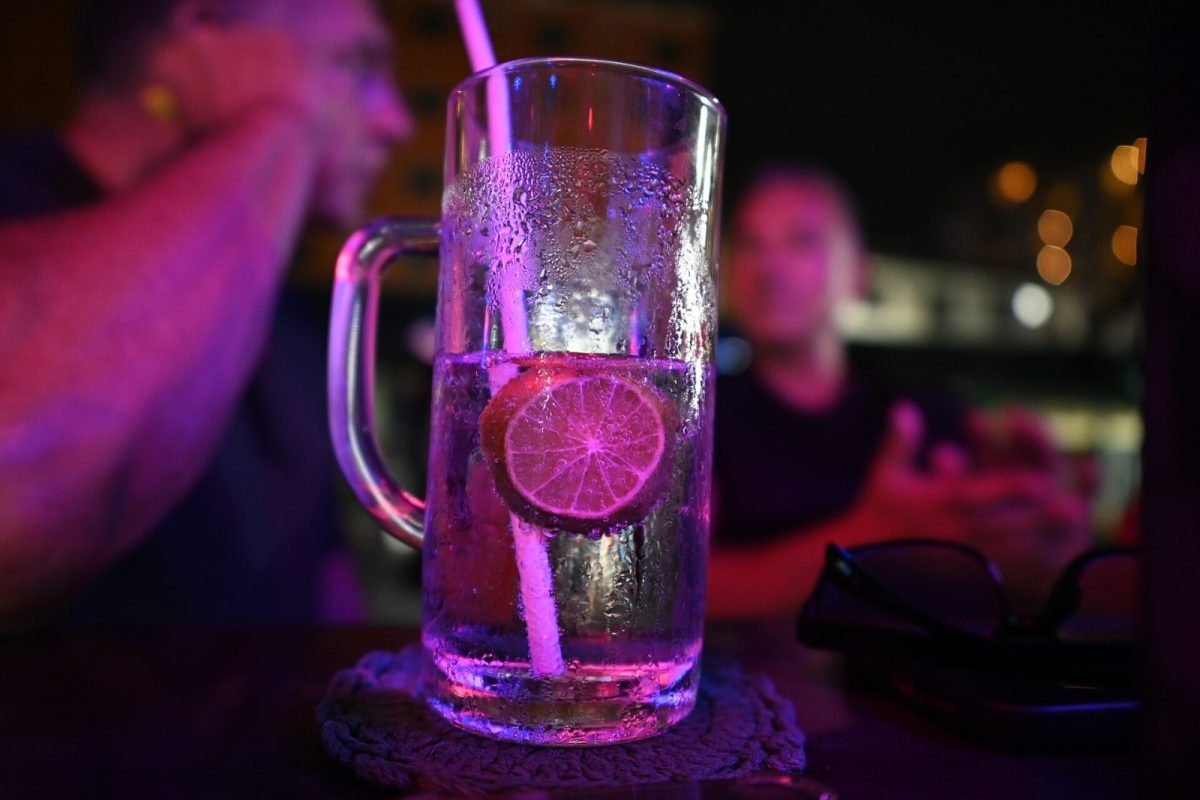 Copa de cóctel con hielo y una rodaja de lima iluminada por luces de neón en un bar nocturno