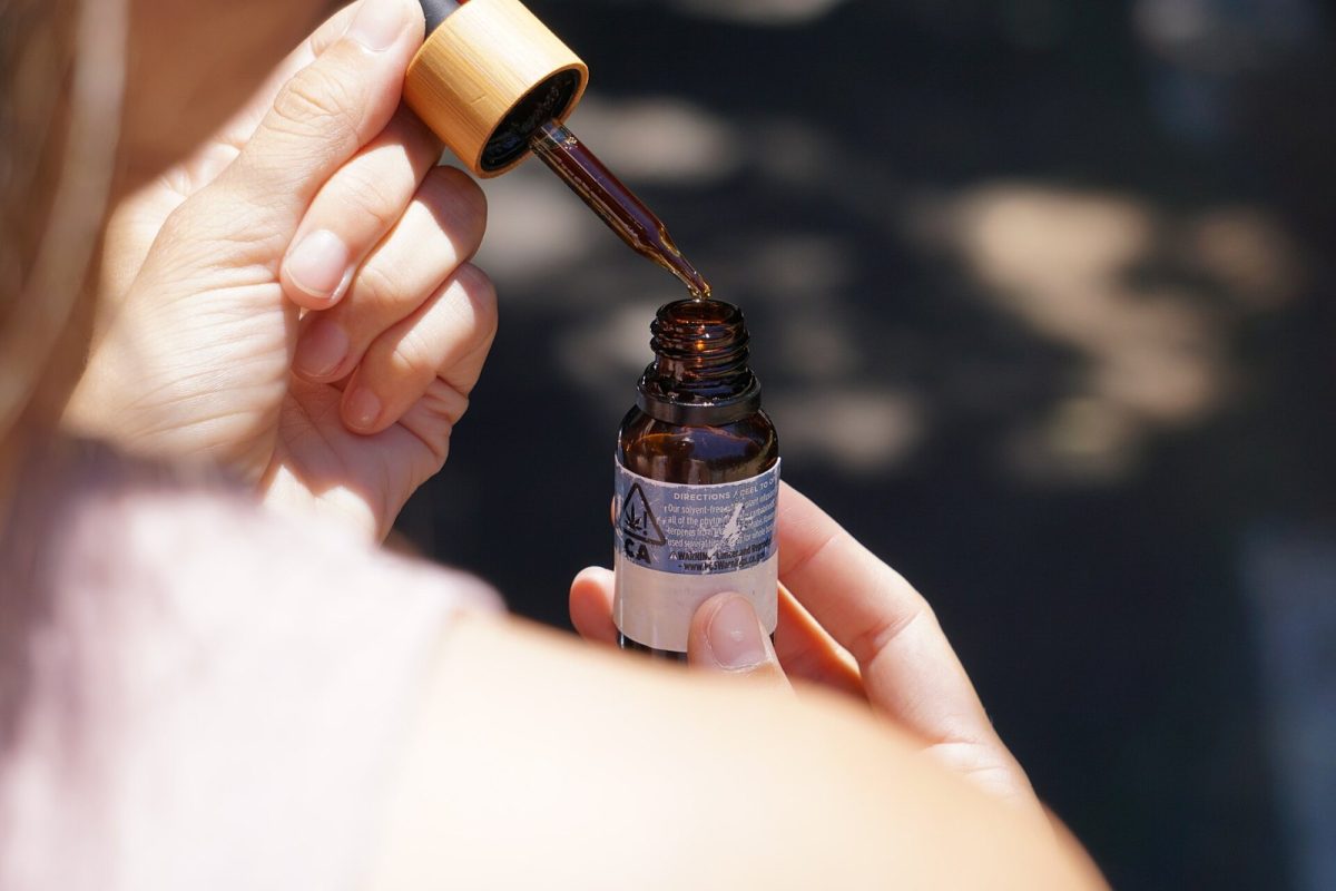 Manos sosteniendo un cuentagotas con aceite de CBD sobre un frasco de vidrio ámbar
