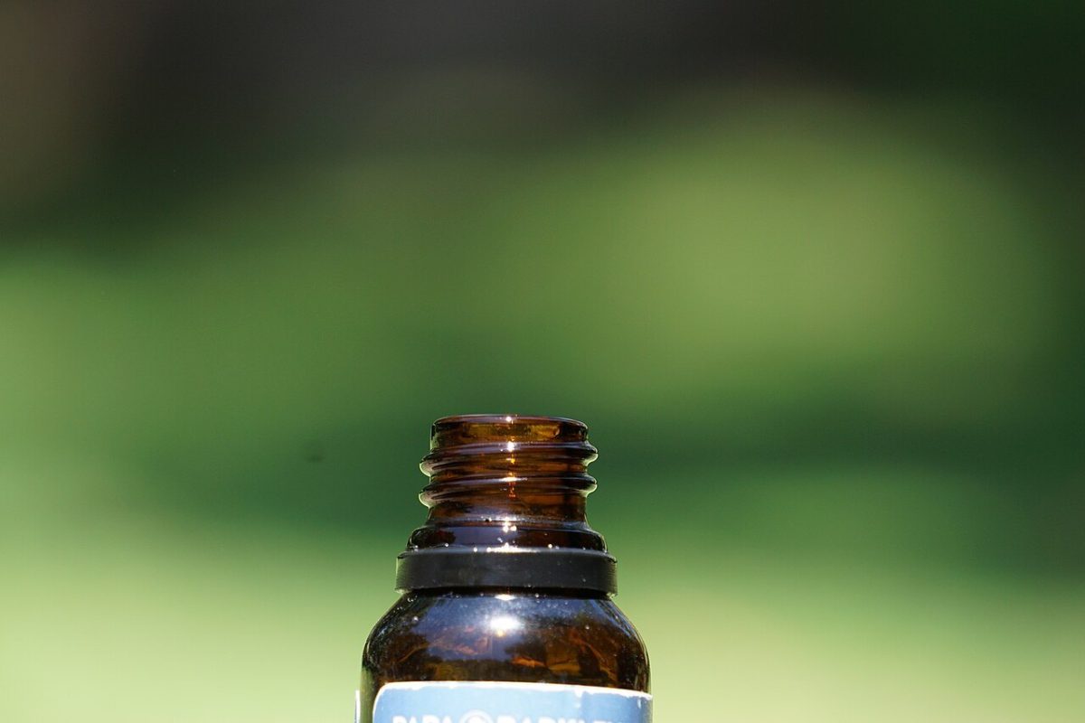 Primer plano del cuello de una botella de vidrio ámbar con gotero, usada para aceite de cáñamo (CBD), sobre fondo verde desenfocado