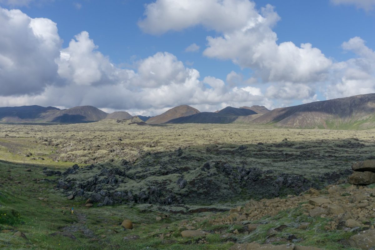 Vasto paisaje volcánico islandés con campos de lava cubiertos de musgo y montañas al fondo bajo un cielo con nubes