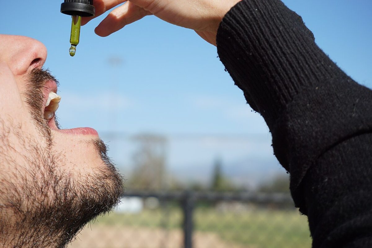 Persona tomando por vía sublingual unas gotas de aceite de cannabis con un gotero, al aire libre