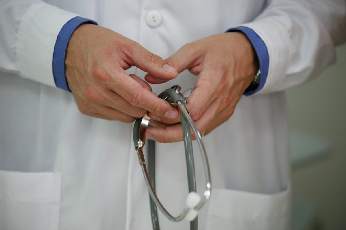 Manos de un médico con bata blanca sosteniendo y ajustando un estetoscopio