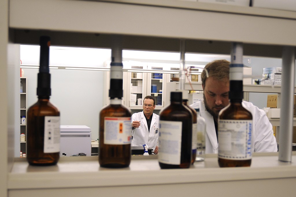 Investigadores con bata blanca trabajando en un laboratorio de toxicología forense, con frascos de reactivos en primer plano