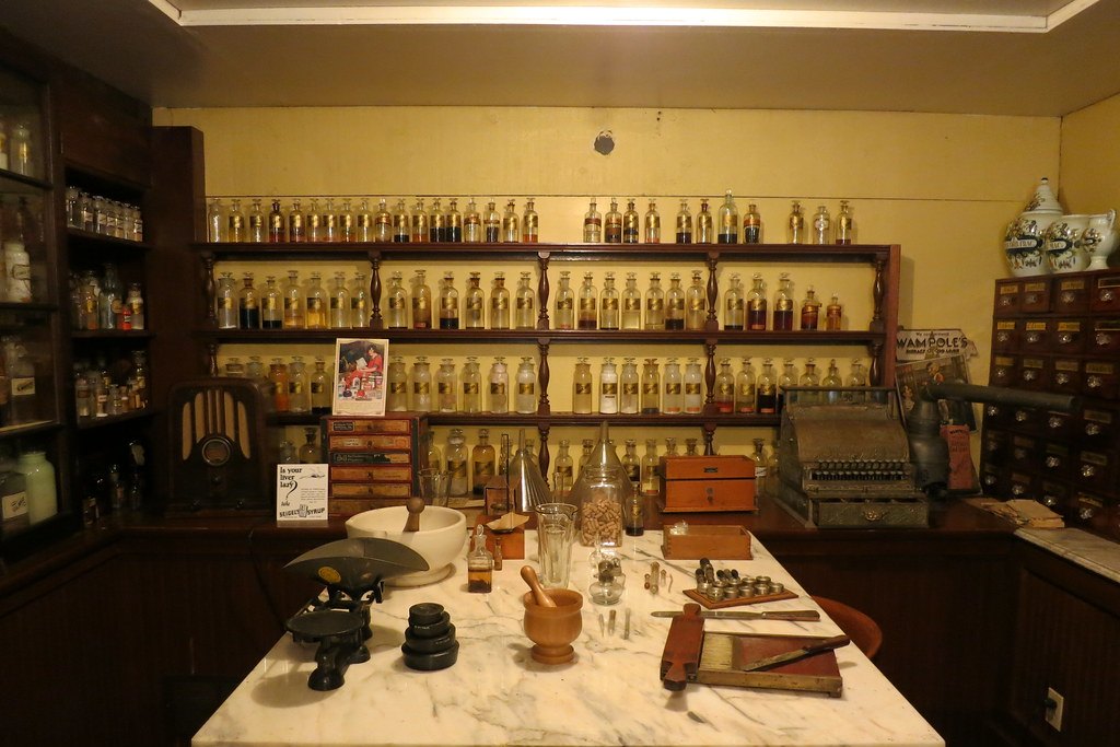 Interior de una antigua droguería, con estanterías llenas de frascos de vidrio, balanza y mortero sobre un mostrador de mármol