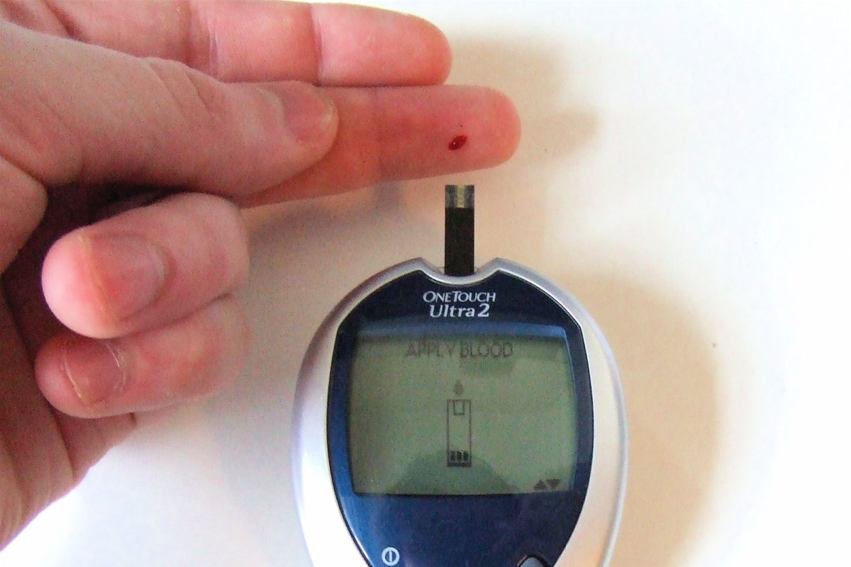Mano sosteniendo un glucómetro digital con una gota de sangre en la punta de un dedo para medir la glucemia