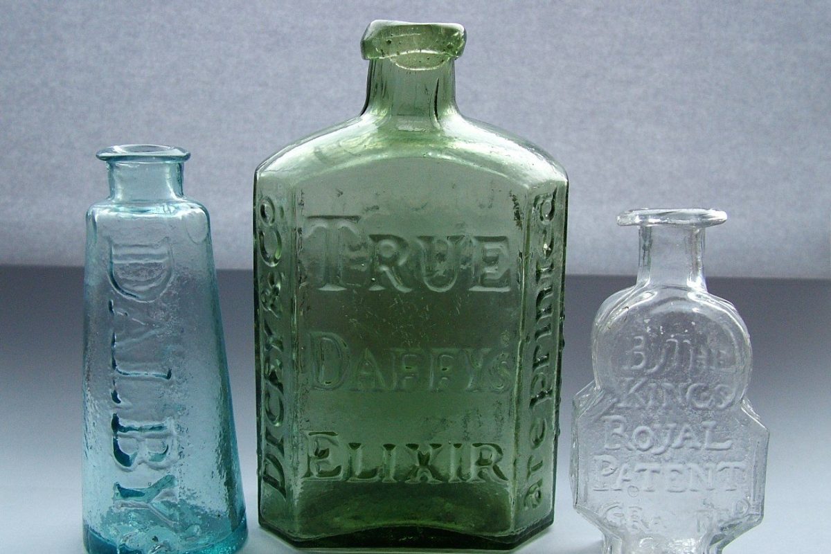 Fotografía de tres antiguos frascos de vidrio de medicinas de patente con textos en relieve, entre ellos "True Daffy's Elixir"