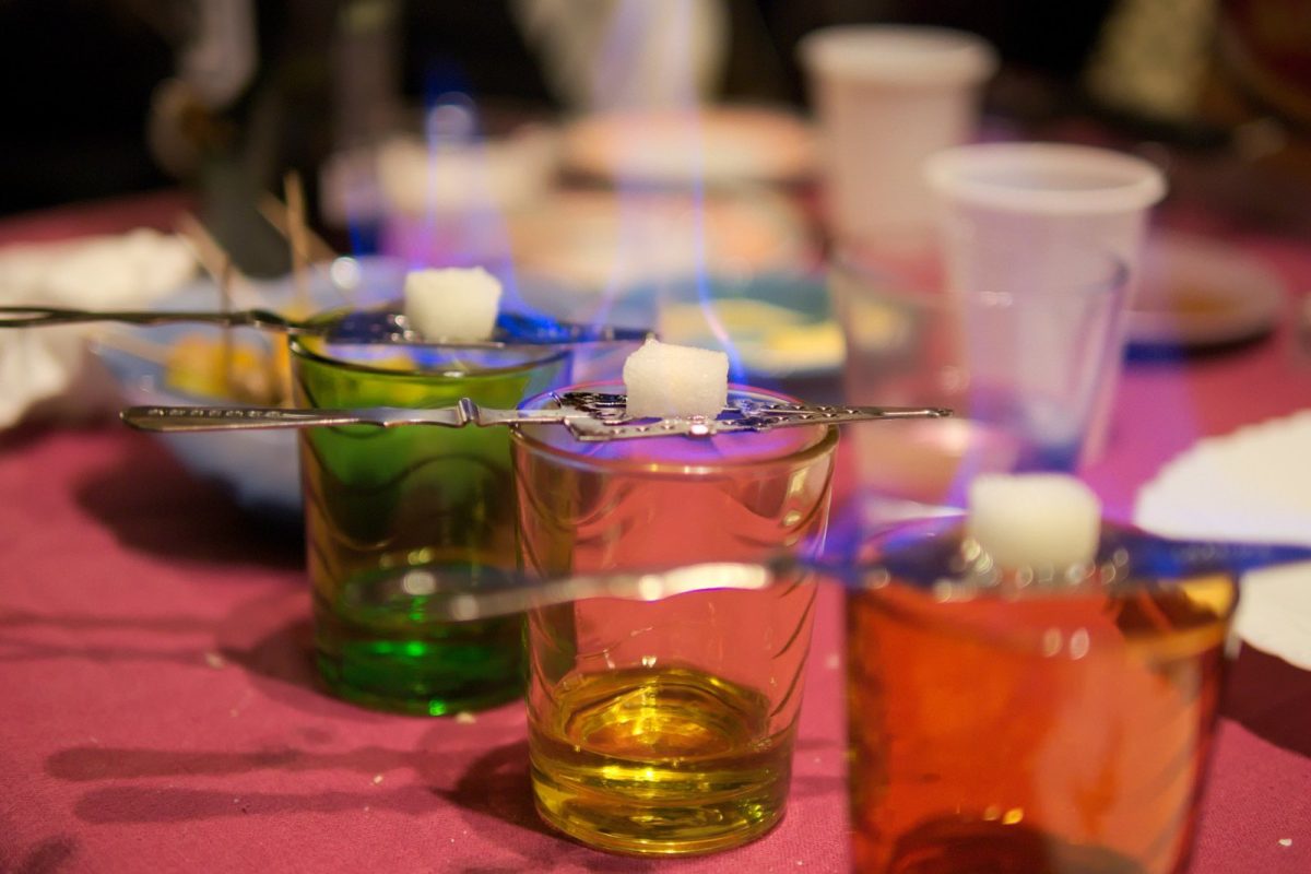 Terrones de azúcar ardiendo sobre vasos de absenta de colores verde, ámbar y rojo, siguiendo el método clásico de preparación