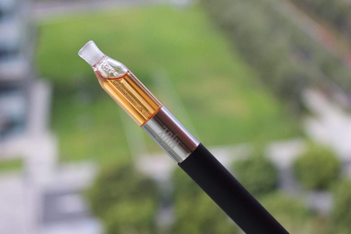 Primer plano de un cartucho de aceite ambarino acoplado a una pluma vaporizadora, con fondo verde desenfocado