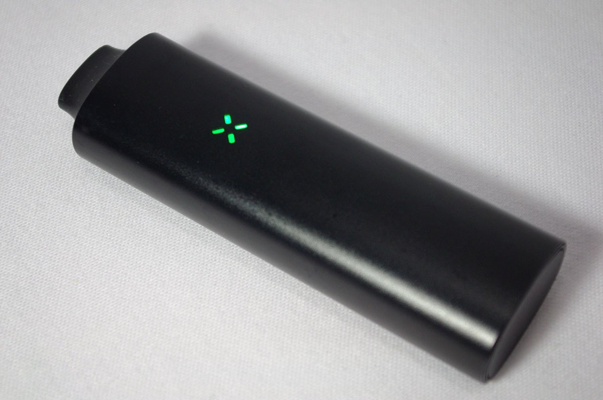 Vaporizador portátil negro de hierba seca con indicador luminoso verde encendido, sobre superficie clara