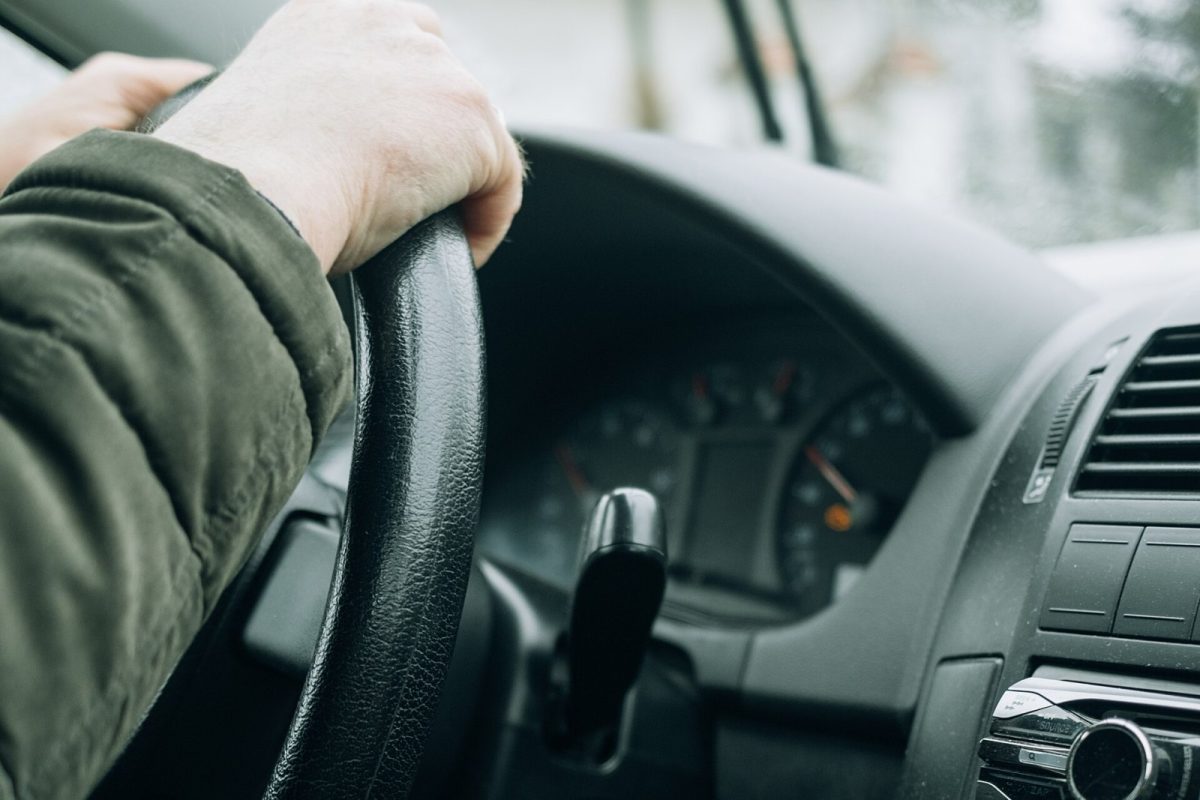 Mano de un conductor sujetando el volante de un coche, con el salpicadero y la carretera nevada al fondo