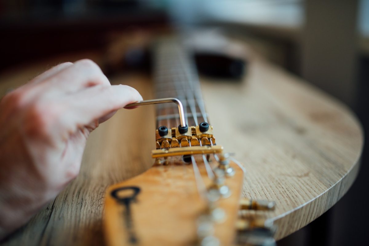 Primer plano de una mano ajustando el puente y las cuerdas de una guitarra eléctrica con una llave hexagonal