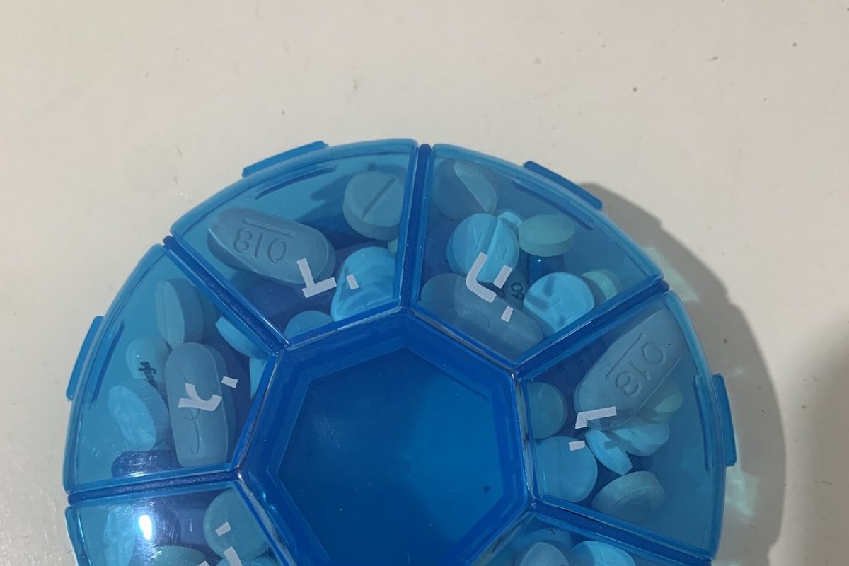 Vista cenital de un pastillero organizador semanal de plástico azul lleno de distintas pastillas y cápsulas