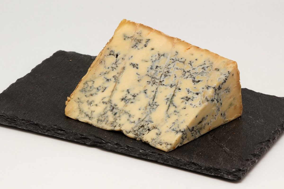 Una cuña de queso Stilton azul con vetas de moho, sobre una tabla de pizarra negra